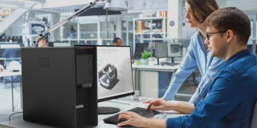 Engineer Talking With Project Manager and Working on Desktop Computer Using CAD Software with Technical Drawings on the Screen. In the Background Engineering Facility Specialising on Industrial Design