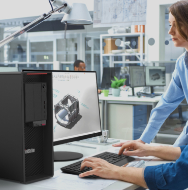 Engineer Talking With Project Manager and Working on Desktop Computer Using CAD Software with Technical Drawings on the Screen. In the Background Engineering Facility Specialising on Industrial Design